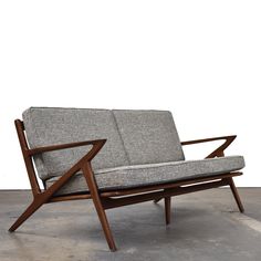 a gray couch sitting on top of a cement floor next to a wooden frame chair