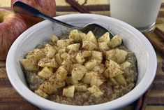 a bowl filled with oatmeal next to two apples and cinnamon sticks on a table