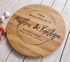 a personalized cutting board next to tomatoes and garlic on a white wooden surface with the words, woodford's matter & kathy established in black ink