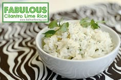 a white bowl filled with rice and garnished with green leafy leaves on a black and white table cloth