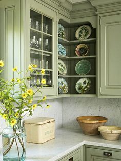 a kitchen with green cabinets and yellow flowers in the vase on the countertop, along with matching plates