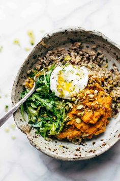 a bowl filled with rice and vegetables on top of a white countertop next to a spoon