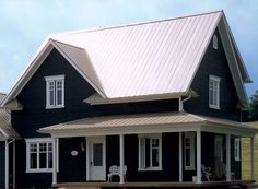 a black house with white trim on the front and side windows, sitting next to a grassy field