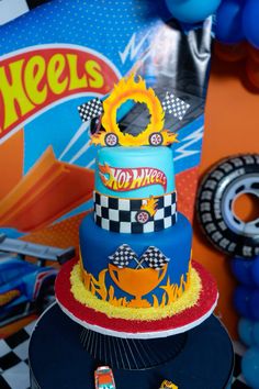 a birthday cake with hot wheels on it and balloons in the background at a race themed birthday party