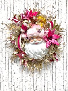 a christmas wreath with a santa claus face and pink flowers on the front, against a white wall