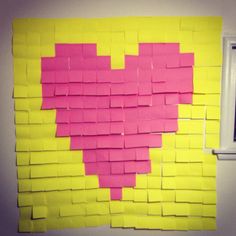 a yellow and pink heart made out of sticky notes on a wall next to a window