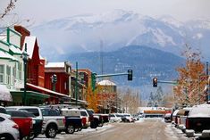 cars are parked on the street in front of snow covered buildings and mountains behind them