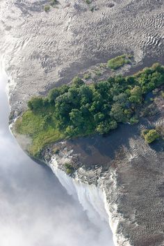 an aerial view of a waterfall surrounded by trees and clouds in the distance is shown