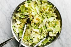 a bowl filled with chopped lettuce and two tongs