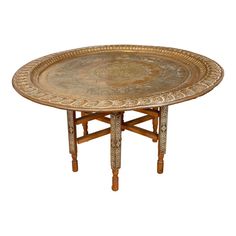 an ornately decorated table with wooden legs and a gold plate on the top, against a white background