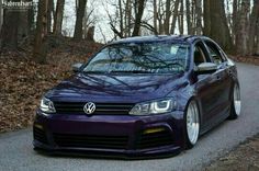 a purple car parked on the side of a road in front of trees and leaves