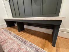 a wooden bench sitting on top of a hard wood floor next to a rug and wall