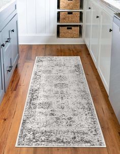 a large rug in the middle of a kitchen with white cabinets and wooden flooring