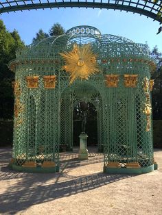 a large green metal structure with gold decorations on it's sides in a park