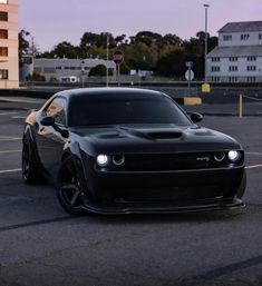 a black sports car parked in a parking lot next to some tall buildings at dusk