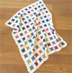 a white crocheted blanket with multicolored flowers on it sitting on top of a wooden floor