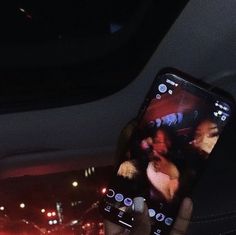 someone is holding up their cell phone in the back seat of a car at night