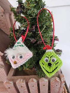 two knitted ornaments hanging from a christmas tree in a wooden sleigh, one green and the other red