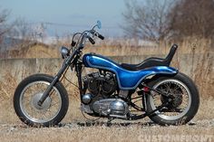 a blue and black motorcycle parked on the side of a road in front of some dry grass