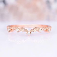 a rose gold wedding ring with three diamonds on it's side, sitting on a white surface