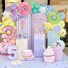 a table topped with lots of balloons and donuts next to a sign that says happy 5th birthday