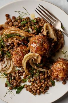 a white plate topped with meat, beans and veggies next to a fork