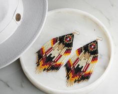 a pair of beaded earrings sitting on top of a white plate next to a hat