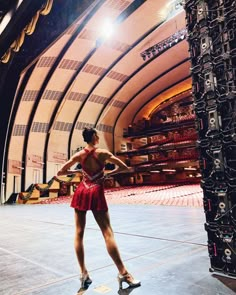 a woman in red dress standing on stage with her hands behind her back and legs crossed