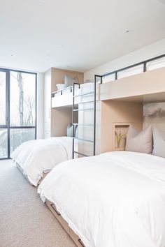 two beds in a room with white sheets and pillows on the bottom bunk, next to a large window