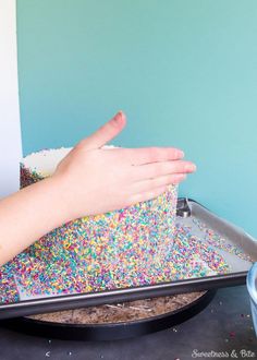 a person reaching for sprinkles on a cake pan with their hand over it