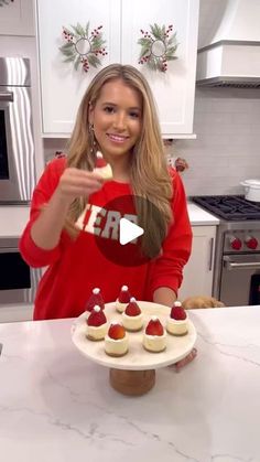 a woman in a red shirt is holding a plate with cupcakes on it