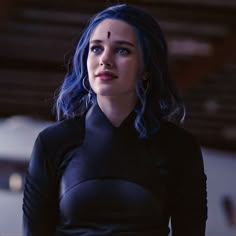 a woman with blue hair wearing a black dress and looking off to the side in a warehouse