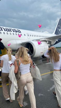 several women are walking towards an airplane on the tarmac with pink hearts attached to it