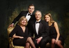 an older man and two younger women pose for a family photo in formal attire, sitting on a gold chair