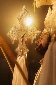 a man standing in front of a white cross with lights on it's head