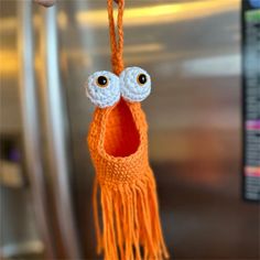 an orange crocheted bird ornament hanging from a hook in front of a refrigerator