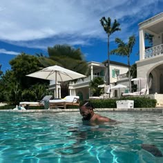 a man swimming in a pool next to a large white house with palm trees and lawn chairs