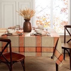 the table is set for two with dishes and cups on it, along with an orange plaid tablecloth