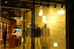 two mannequins in front of a store window at night with lights on