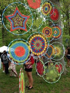 a woman standing next to a tree filled with lots of colorful kites on top of green grass