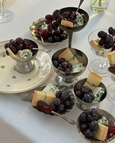 grapes, cheese and crackers are arranged in bowls on a table with wine glasses