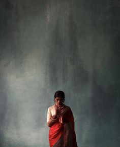 a woman in a red sari standing with her hands clasped up to her chest