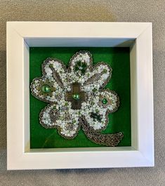 a white frame holding a green and white brooch in it's center, surrounded by beads