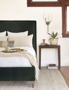 a bed with pillows and blankets on it in a bedroom next to a table, mirror and lamp