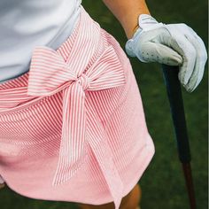 a woman holding a golf club and wearing a pink skirt with a bow on it