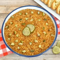 a bowl filled with food next to some bread and cucumbers on a red checkered table cloth