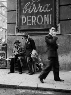 an old black and white photo of people on the sidewalk