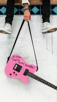 a pink guitar hanging from the side of a building with writing on it that says tickets to my downfall