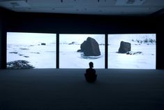 a person sitting on the floor in front of three large screens with snow covered rocks