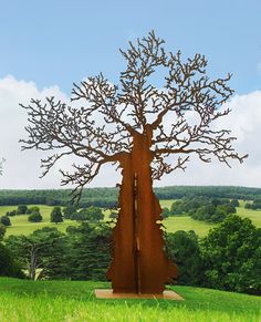 a large metal tree sculpture in the middle of a grassy field with trees behind it